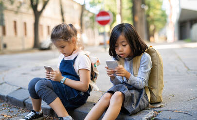 Kleine Mädchen mit Smartphones sitzen in der Stadt im Freien und spielen Online-Spiele. - HPIF15427