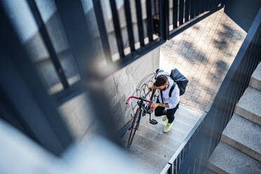 Portrait of young man commuter with headphones and bicycle walking outdoors in city. - HPIF15438