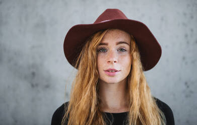 Nahaufnahme eines Porträts einer jungen Frau mit roten Haaren und Hut vor grauem Hintergrund. - HPIF15441