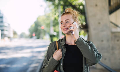 Front view portrait of cheerful young woman with red hair outdoors in town, using smartphone. - HPIF15446