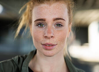 Close-up front view portrait of young woman with red hair outdoors in town, looking at camera. - HPIF15450