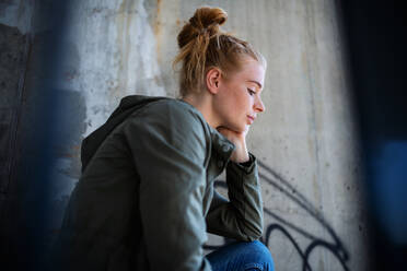 Portrait of sad young woman with red hair outdoors in town, sitting and resting on staircase. - HPIF15455