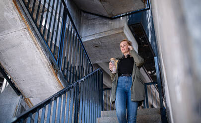 Porträt einer jungen Frau mit roten Haaren, die draußen in der Stadt eine Treppe hinuntergeht und ein Smartphone benutzt. - HPIF15458
