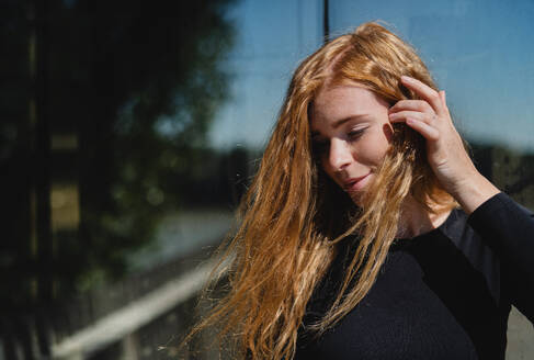 Portrait of young woman with red hair and closed eyes outdoors in town. Copy space. - HPIF15463
