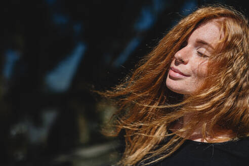 Portrait of young woman with red hair and closed eyes outdoors in town. Copy space. - HPIF15464