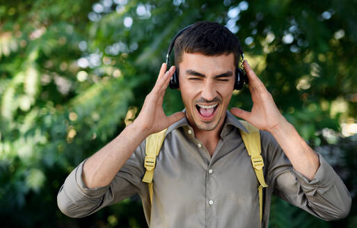 Porträt eines jungen attraktiven Mannes mit Kopfhörern, der in der Stadt im Freien steht und singt. - HPIF15467