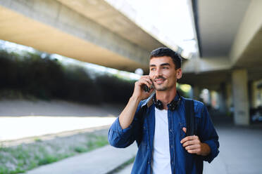 Porträt eines jungen attraktiven Mannes mit Kopfhörern und Smartphone beim Spaziergang in der Stadt. - HPIF15469