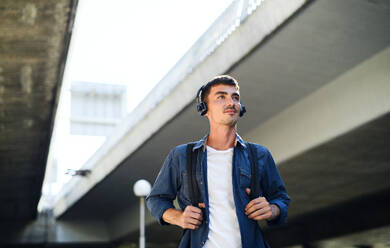 Niedriger Blickwinkel auf einen jungen, attraktiven Mann mit Kopfhörern, der im Freien in einer Stadt steht. Raum kopieren. - HPIF15470