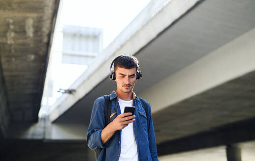 Niedriger Blickwinkel auf einen jungen, attraktiven Mann mit Kopfhörern, der im Freien in einer Stadt steht. Raum kopieren. - HPIF15472