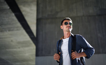 Low-angle view of young attractive man with backpack standing outdoors in city. Copy space. - HPIF15477