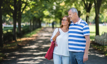 Front view portrait of happy senior couple walking outdoors in city or town park. - HPIF15484