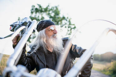 Ein älterer Mann mit Motorrad und Sonnenbrille auf dem Lande. - HPIF15489