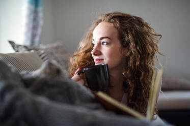 Young woman relaxing indoors at home with book and cup of coffee or tea. - HPIF15493