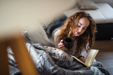 Junge Frau entspannt sich zu Hause mit Kaffee und Buch. - HPIF15494