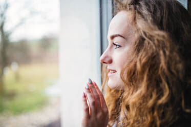 Nahaufnahme eines Porträts einer jungen Frau, die zu Hause am Fenster steht, Kopierraum. - HPIF15503