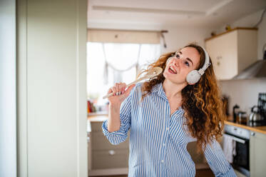 Young woman with headphones relaxing indoors at home, listening to music and singing. - HPIF15504