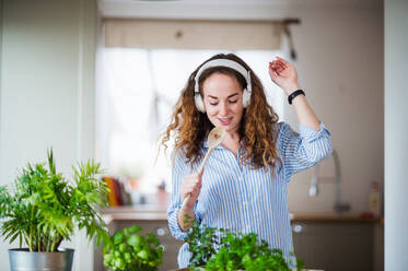 Young woman with headphones relaxing indoors at home, listening to music and singing. - HPIF15505