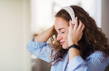 Junge Frau mit Kopfhörern, die sich zu Hause entspannt und Musik hört. - HPIF15507