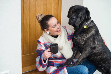 Junge Frau entspannt sich im Freien vor der Haustür mit Kaffee und Hund. - HPIF15513