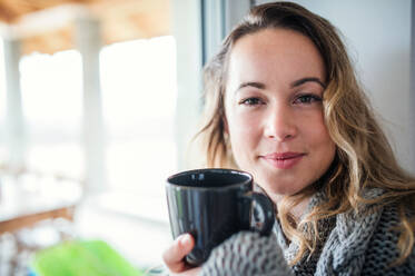 Vorderansicht einer jungen Frau, die sich zu Hause mit einer Tasse Kaffee oder Tee entspannt. - HPIF15520