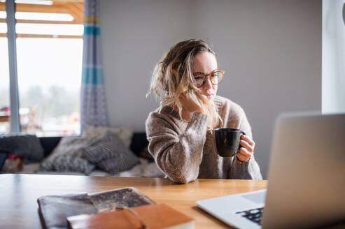 Porträt einer jungen Frau mit Laptop und Kaffee bei der Arbeit zu Hause. - HPIF15525