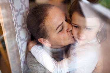 Ältere Großmutter küsst ihre kleine Enkelin zu Hause, Aufnahme durch Glas. - HPIF15549