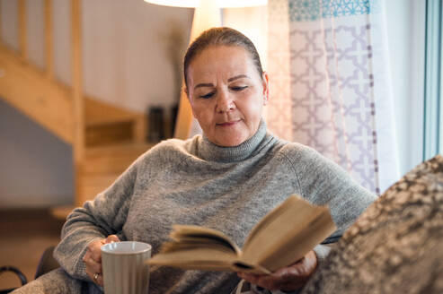 Vorderansicht Porträt einer älteren Frau, die zu Hause auf dem Sofa sitzt und ein Buch liest. - HPIF15550