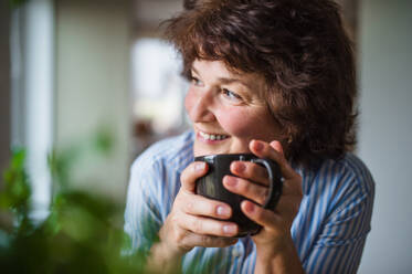 Portrait of senior woman with cup of coffee at home, relaxing. - HPIF15563