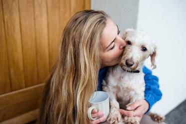 Reife Frau entspannt sich im Freien vor der Haustür mit Kaffee und Hund, küssend. - HPIF15568