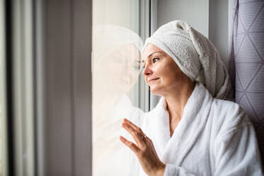 Portrait of lonely woman with bathrobe and towel on head standing indoors at home. - HPIF15577