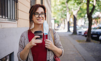 Portrait of mature woman with coffee walking outdoors in city or town, coronavirus concept. - HPIF15584