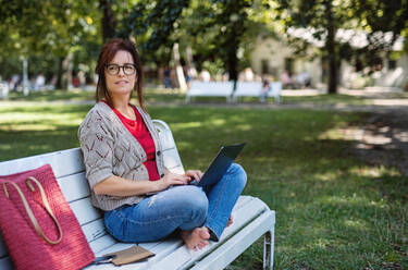 Reife Frau mit Laptop im Freien in einem Stadtpark bei der Arbeit, Raum kopieren. - HPIF15590