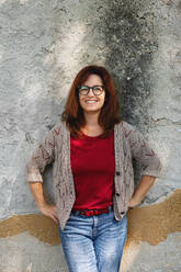 Portrait of mature woman standing outdoors in city or town against gray wall, looking at camera. - HPIF15592