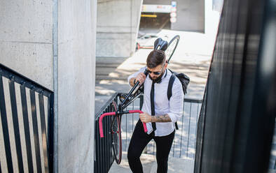 Porträt eines jungen Mannes, der mit Kopfhörern und Fahrrad im Freien in der Stadt spazieren geht. - HPIF15599