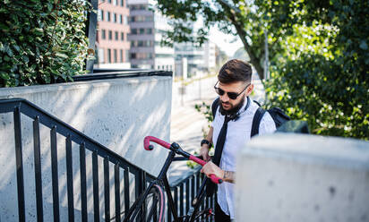 Porträt eines jungen Mannes, der mit Kopfhörern und Fahrrad im Freien in der Stadt spazieren geht. - HPIF15600