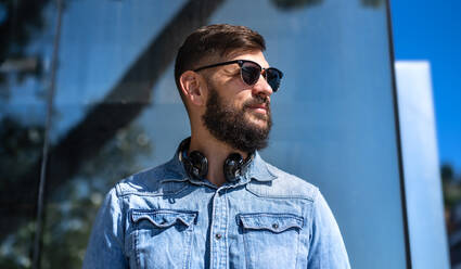 Porträt eines jungen Mannes mit Kopfhörern, der in der Stadt im Freien steht. - HPIF15606