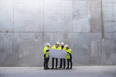 Eine Gruppe von Ingenieuren, die auf einer Baustelle an einer Betonwand stehen und Baupläne in der Hand halten; Raum kopieren. - HPIF15609