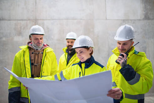 A group of engineers standing against concrete wall on construction site, holding blueprints. - HPIF15613