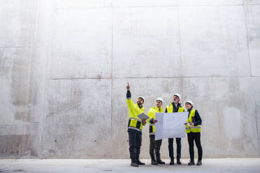 Eine Gruppe von Ingenieuren, die auf einer Baustelle an einer Betonwand stehen und Baupläne in der Hand halten; Raum kopieren. - HPIF15618