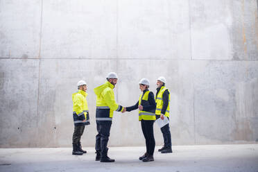 A group of engineers standing on construction site, shaking hands. Copy space. - HPIF15620