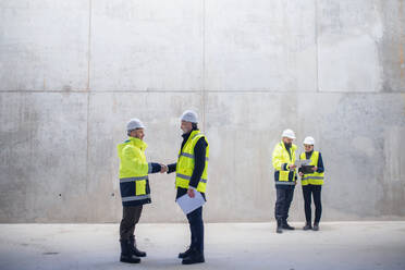 Eine Gruppe von Ingenieuren steht auf einer Baustelle und schüttelt sich die Hände. Raum kopieren. - HPIF15621