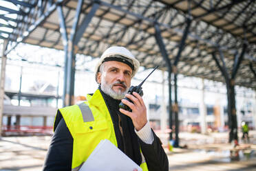 Ein Ingenieur benutzt ein Walkie-Talkie im Freien auf einer Baustelle. - HPIF15629