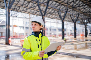 Eine Frau, die als Ingenieurin mit einem Tablet auf einer Baustelle steht und arbeitet. Raum kopieren. - HPIF15631