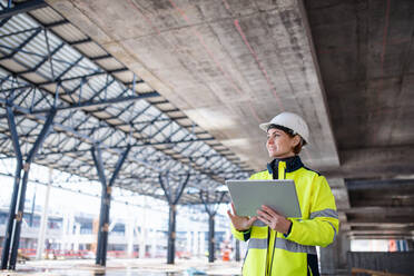 Eine Frau, die als Ingenieurin mit einem Tablet auf einer Baustelle steht und arbeitet. Raum kopieren. - HPIF15633