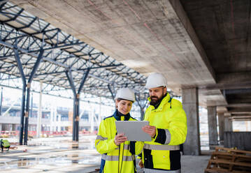 Front view of man and woman engineers standing outdoors on construction site, using tablet. Copy space. - HPIF15634