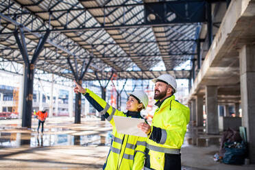 Engineers standing and talking outdoors on construction site, holding tablet. - HPIF15635