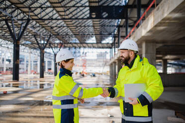 Two engineers with tablet standing on construction site, shaking hands. - HPIF15636