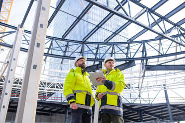 Vorderansicht von Ingenieuren, die im Freien auf einer Baustelle stehen und ein Tablet benutzen. - HPIF15638