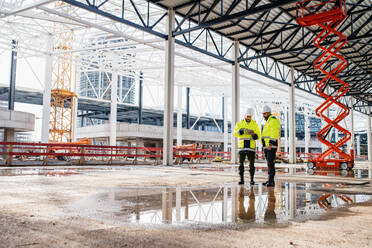 Front view of men engineers standing outdoors on construction site, using tablet. Copy space. - HPIF15639