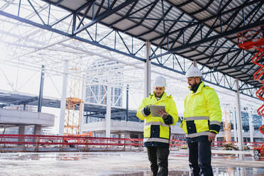 Men engineers standing outdoors on construction site, using tablet. Copy space. - HPIF15640